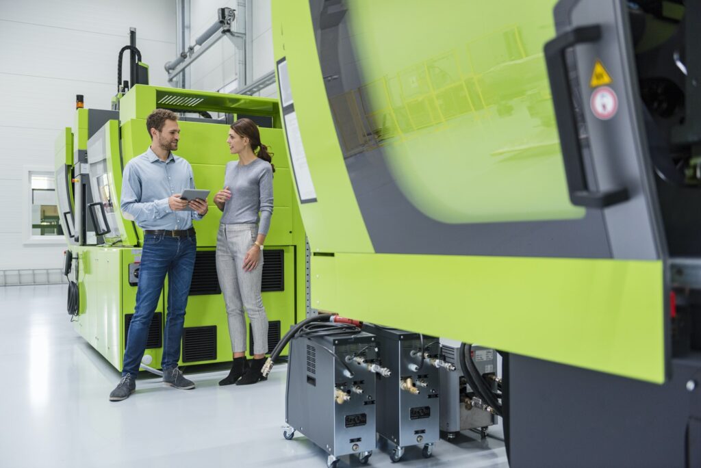 Colleagues in high tech company controlling manufacturing machines, using digital tablet